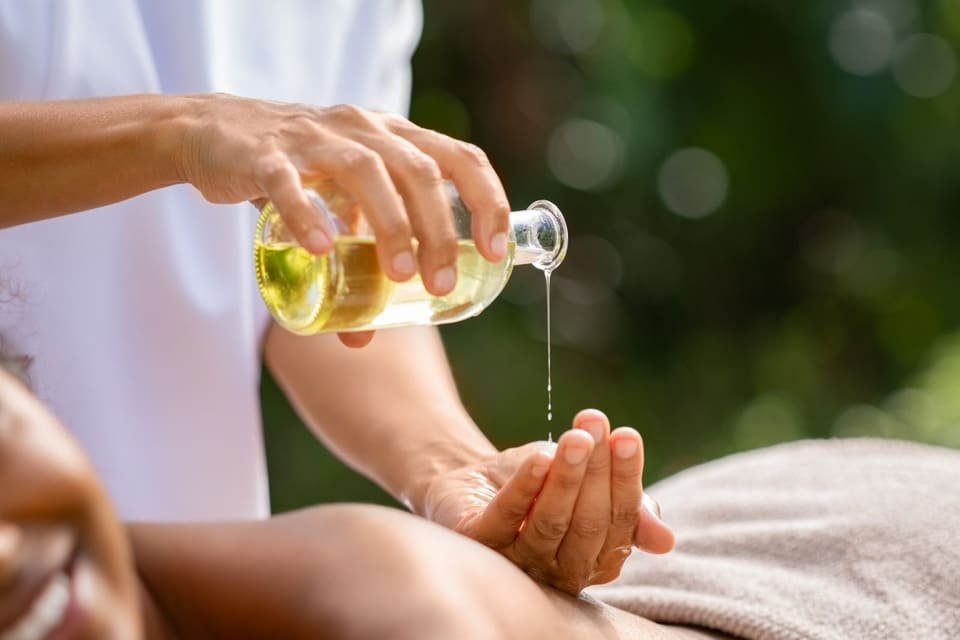 Warm massage oil being poured into a therapist's hands